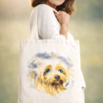 Tote-bag écru peint à la main avec portrait de chien yorkshire, porté par une femme élégante dans un champ ensoleillé.
